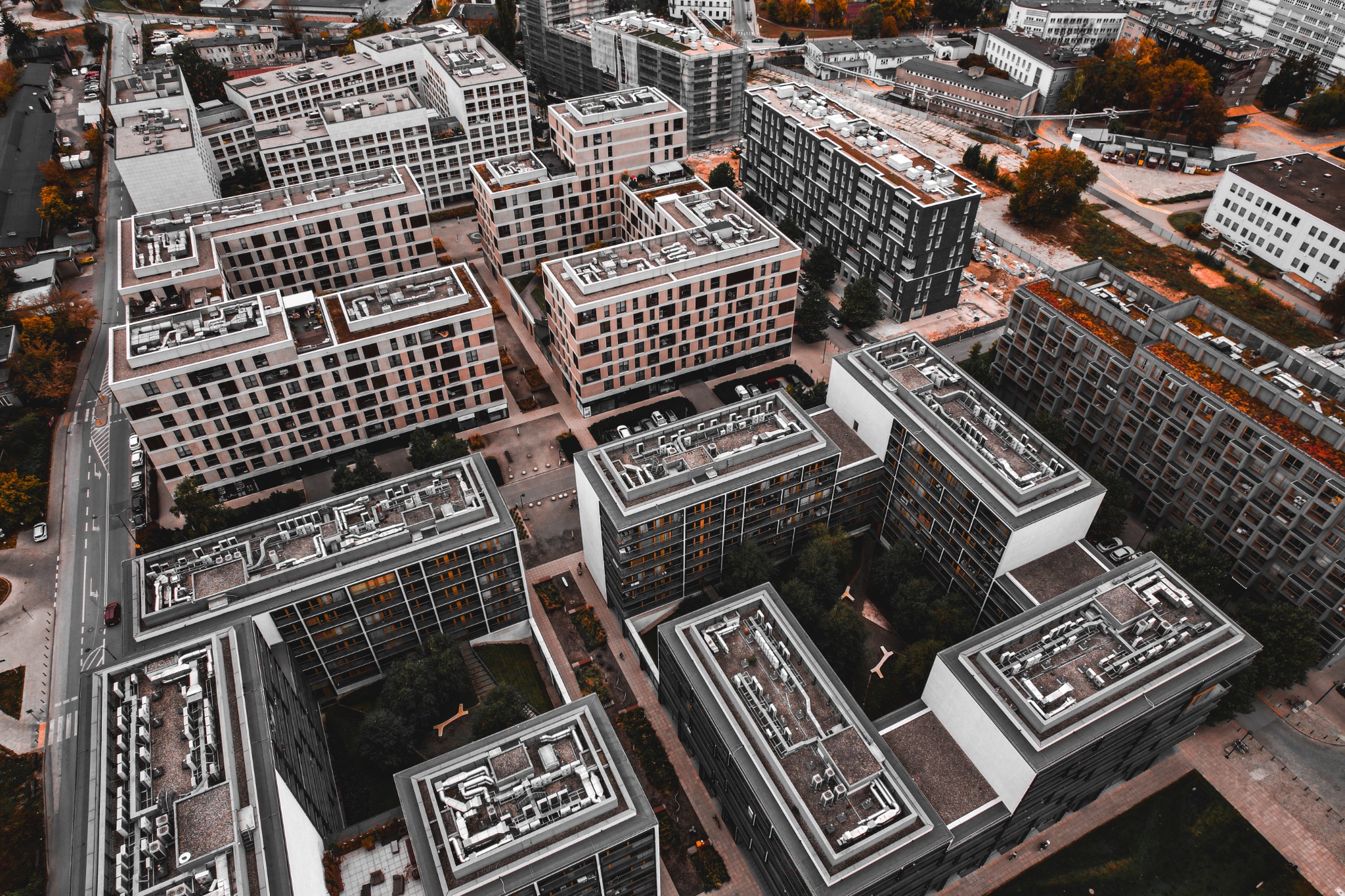 Widok z lotu ptaka na kompleks nowoczesnych budynków mieszkalnych z płaskimi dachami i licznymi oknami, otoczonych zielenią i infrastrukturą miejską.