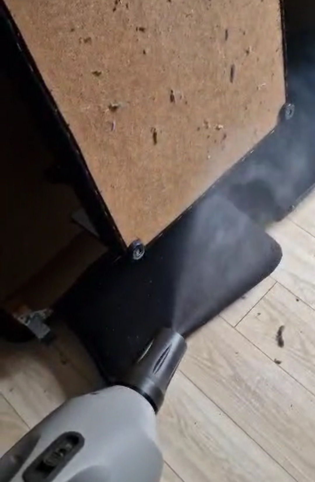 Parownica czyszcząca tapicerkę z bliska, widoczne drewniane elementy mebla i jasna podłoga.