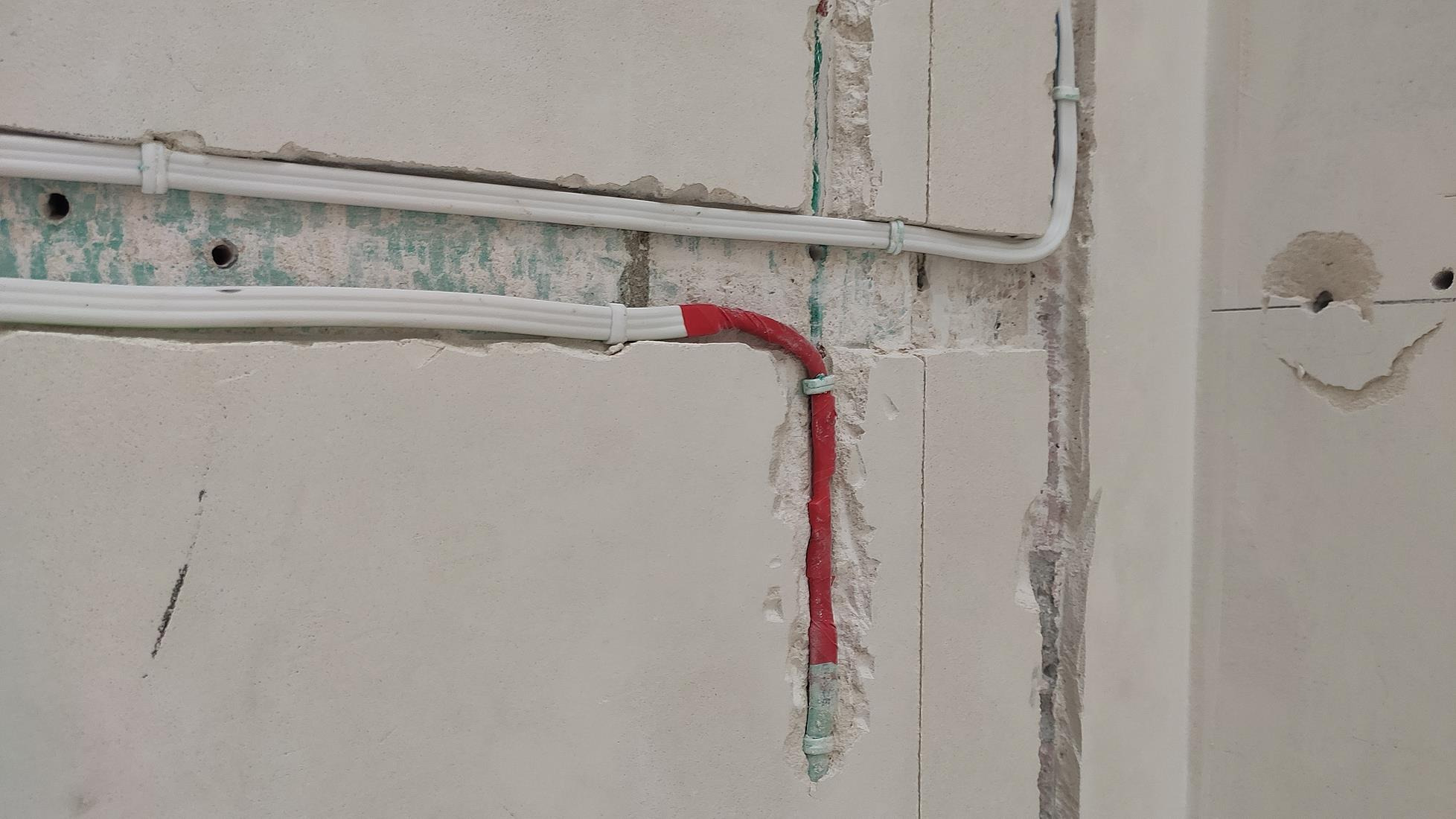 Instalacja elektryczna: białe kable w peszlu i czerwony kabel w ścianie z betonu komórkowego, zabezpieczony czerwoną taśmą izolacyjną.