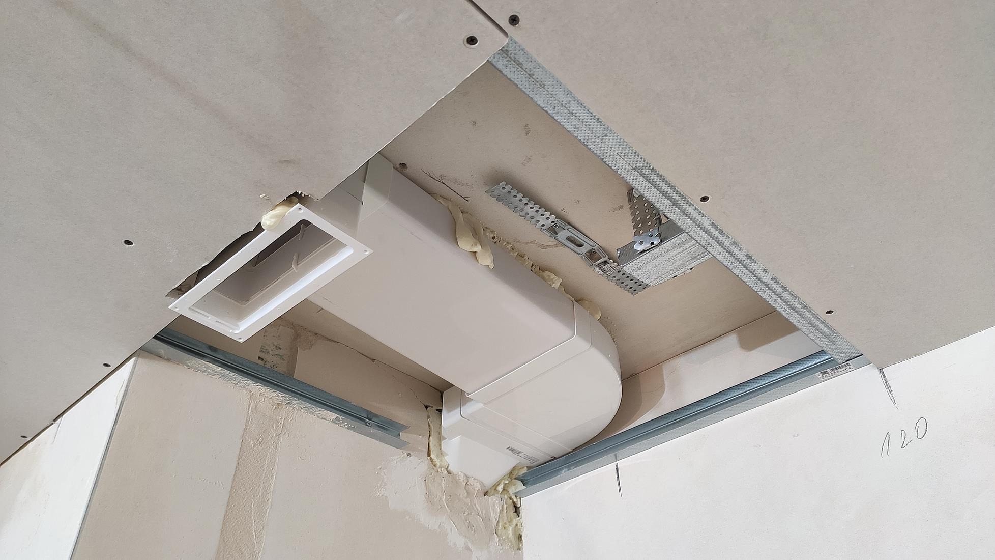Montaż kanału wentylacyjnego pod sufitem z płyt kartonowo-gipsowych, widoczne profile metalowe i pianka montażowa uszczelniająca połączenia.