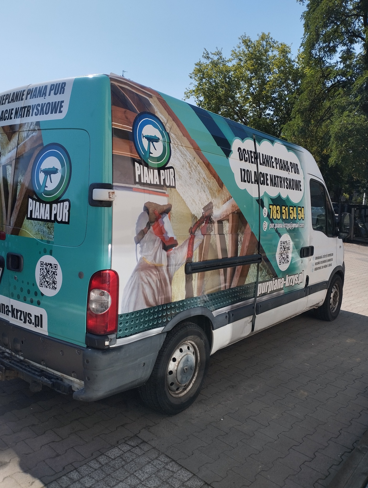 Reklamowy bus z grafiką: ocieplanie pianą PUR, izolacje natryskowe. Widoczne logo, numer telefonu, adres strony internetowej i QR kod firmy.