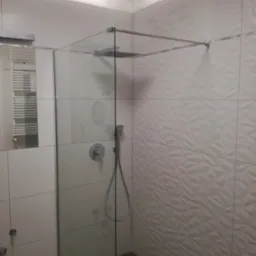 Nowoczesna kabina prysznicowa z deszczownicą i baterią termostatyczną, ściany wyłożone białymi płytkami o trójwymiarowej strukturze, widoczny odpływ liniowy w podłodze.