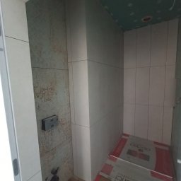 Usługi remontowo budowlane, hydrauliczne i elektryczne. - Wykończona kabina prysznicowa z szarą mozaiką i jasnymi płytkami. Widoczne elementy instalacji podtynkowej i zabezpieczone podłoże. Sufit przygotowany pod malowanie.