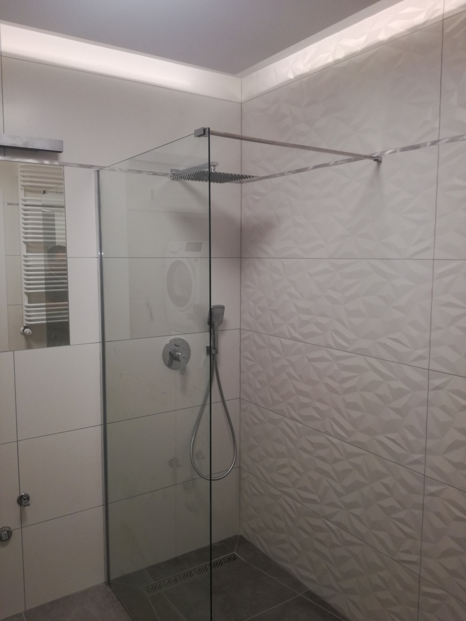 Nowoczesna kabina prysznicowa z deszczownicą i baterią termostatyczną, ściany wyłożone białymi płytkami o trójwymiarowej strukturze, widoczny odpływ liniowy w podłodze.