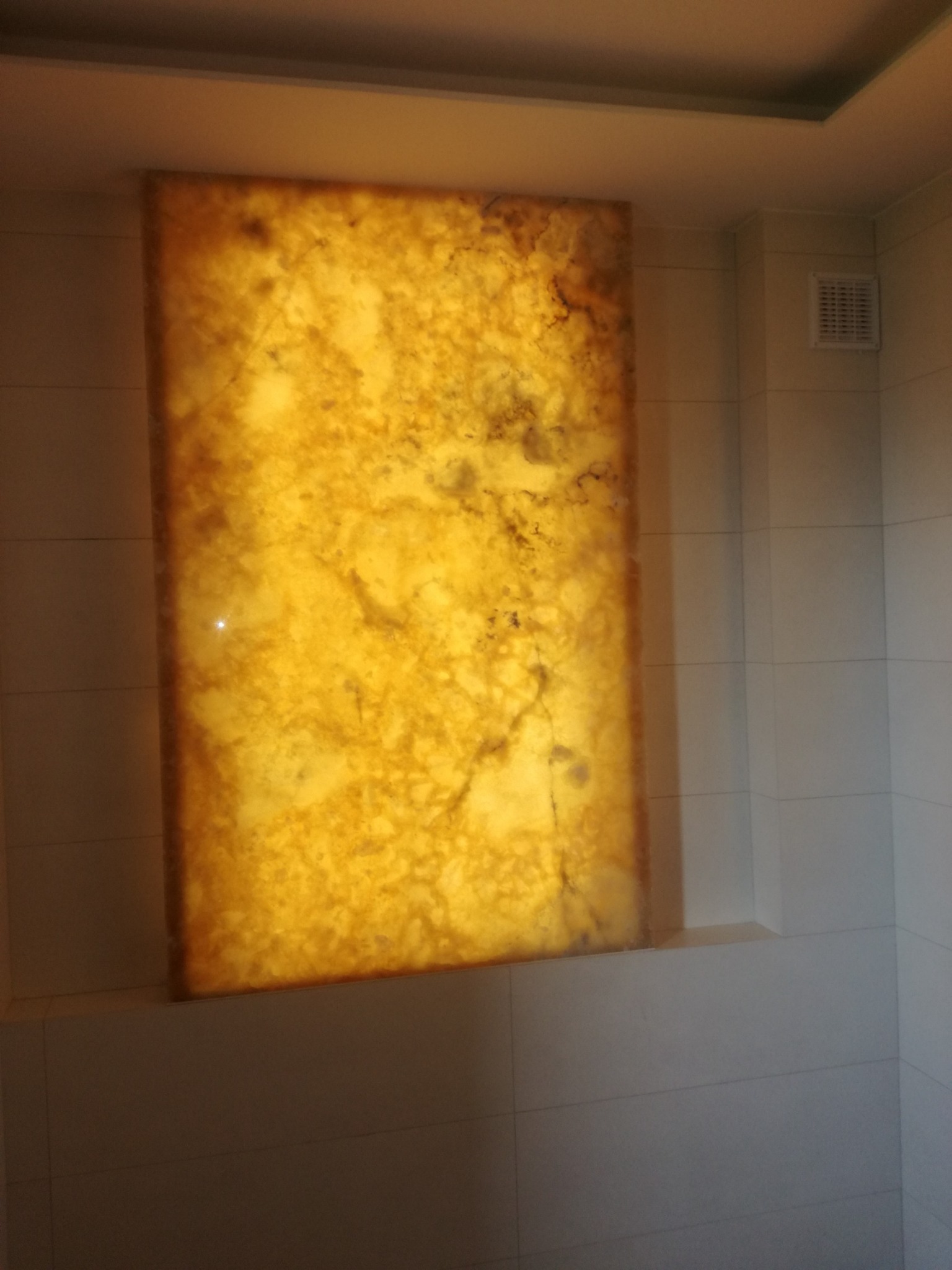 Podświetlony panel z onyksu w łazience, imitujący okno, z widoczną strukturą kamienia i ciepłym światłem.