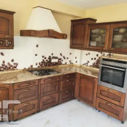 Kuchnia z brązowymi, drewnianymi szafkami, blatem z marmuru i szklanym panelem ściennym z motywem ziaren kawy, wykończona w stylu klasycznym.