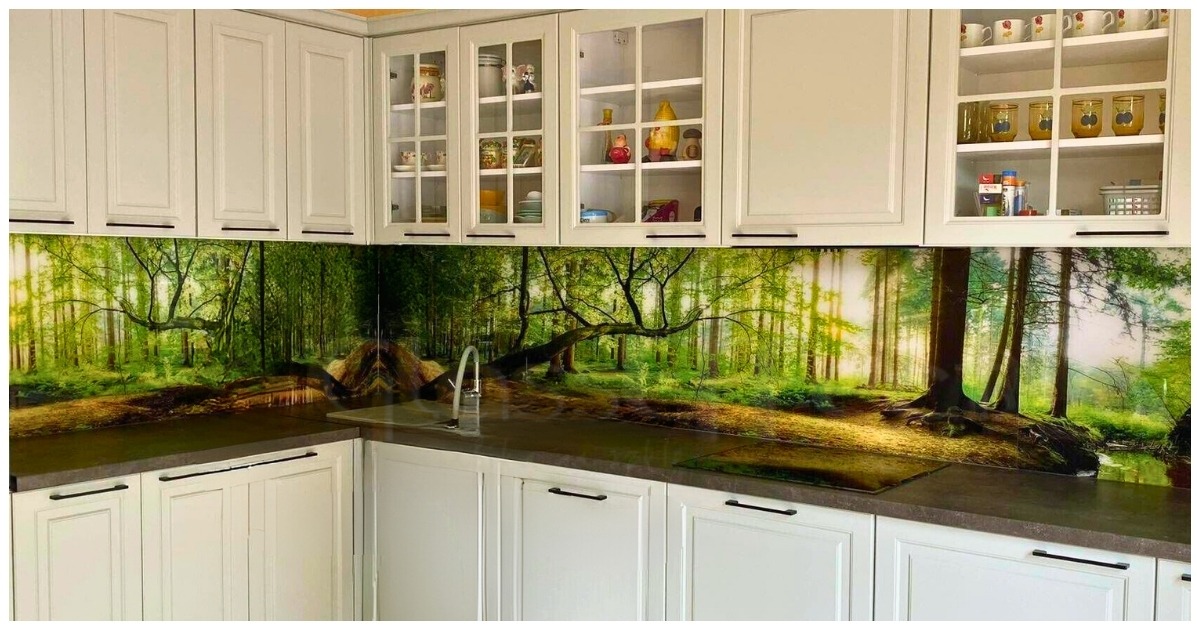 Szklany panel ścienny w kuchni z motywem leśnym, białe szafki z czarnymi uchwytami, przeszklone szafki górne z dekoracyjnymi przedmiotami.