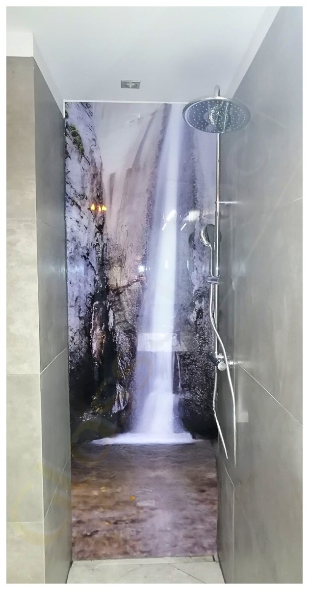 Szklana ściana w kabinie prysznicowej z motywem wodospadu, chromowana bateria prysznicowa z deszczownicą, szare płytki na ścianach.