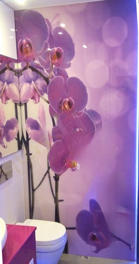 Szklana ściana w łazience z motywem fioletowych orchidei, widoczny fragment toalety i umywalki z różową szafką.