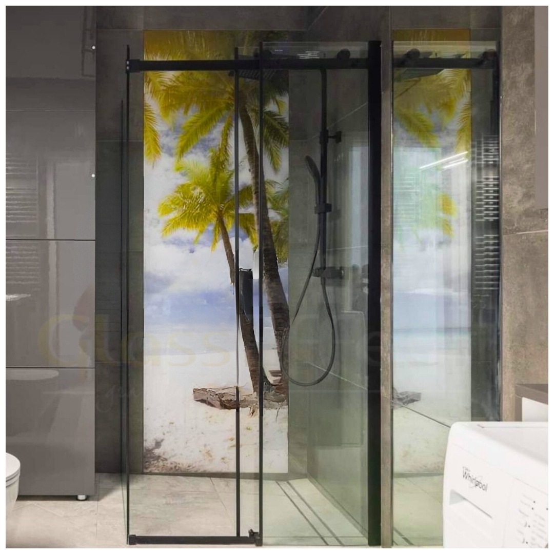 Szklana kabina prysznicowa z czarnymi profilami i grafiką plaży z palmami na tylnej ściance, widoczna pralka i szara zabudowa łazienkowa.