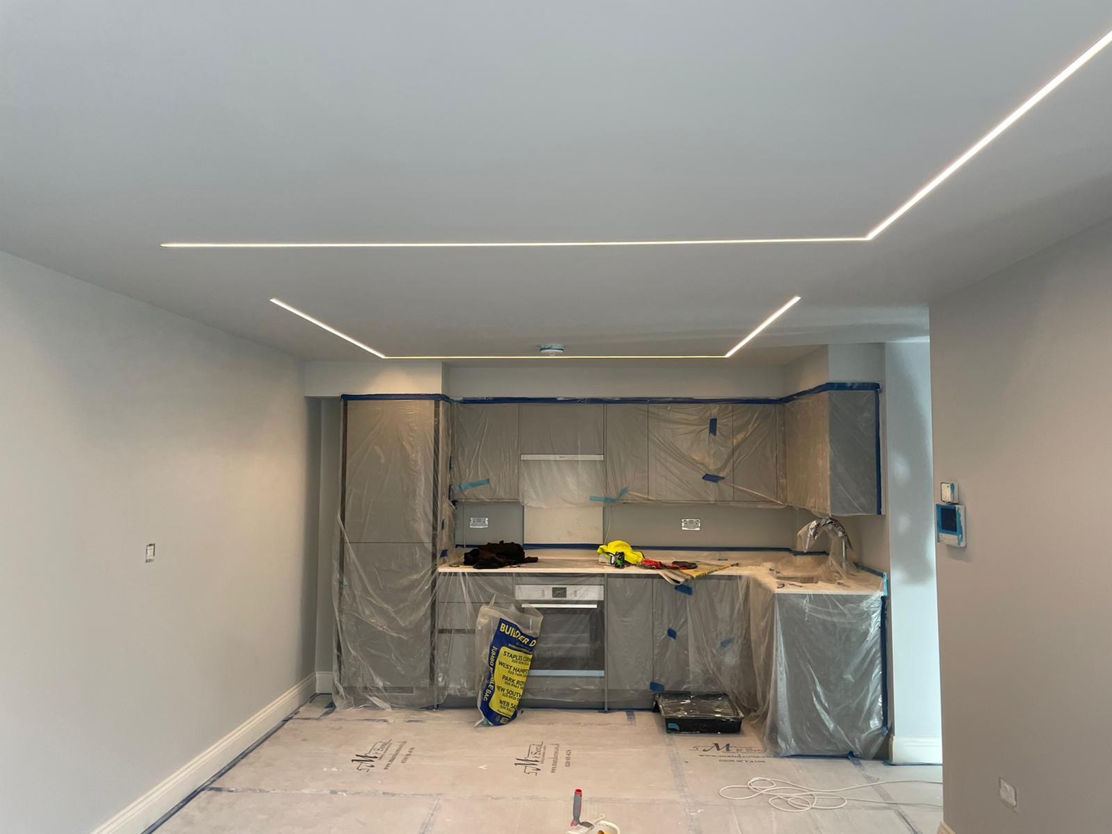 Kuchnia w trakcie remontu, meble zabezpieczone folią, w suficie zamontowane nowoczesne, liniowe oświetlenie LED.