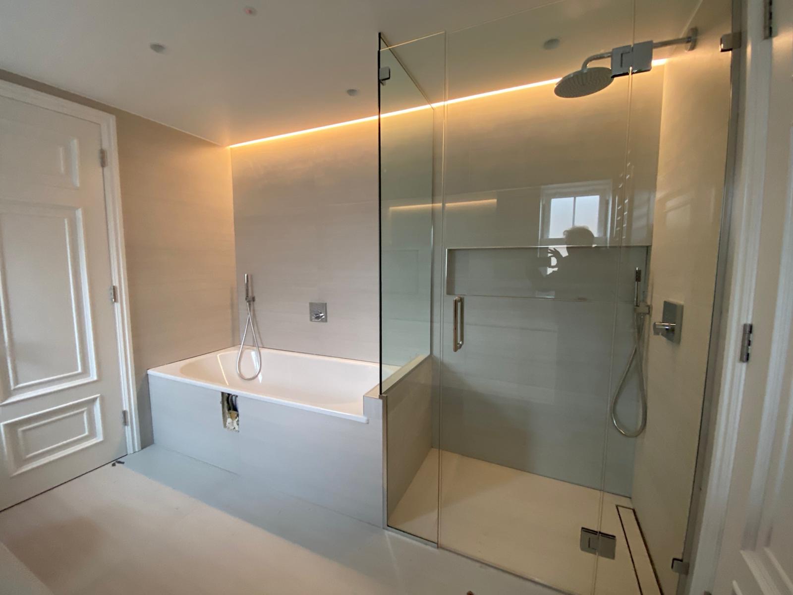 Nowoczesna łazienka z podświetleniem LED nad wanną i kabiną prysznicową ze szklanymi drzwiami.