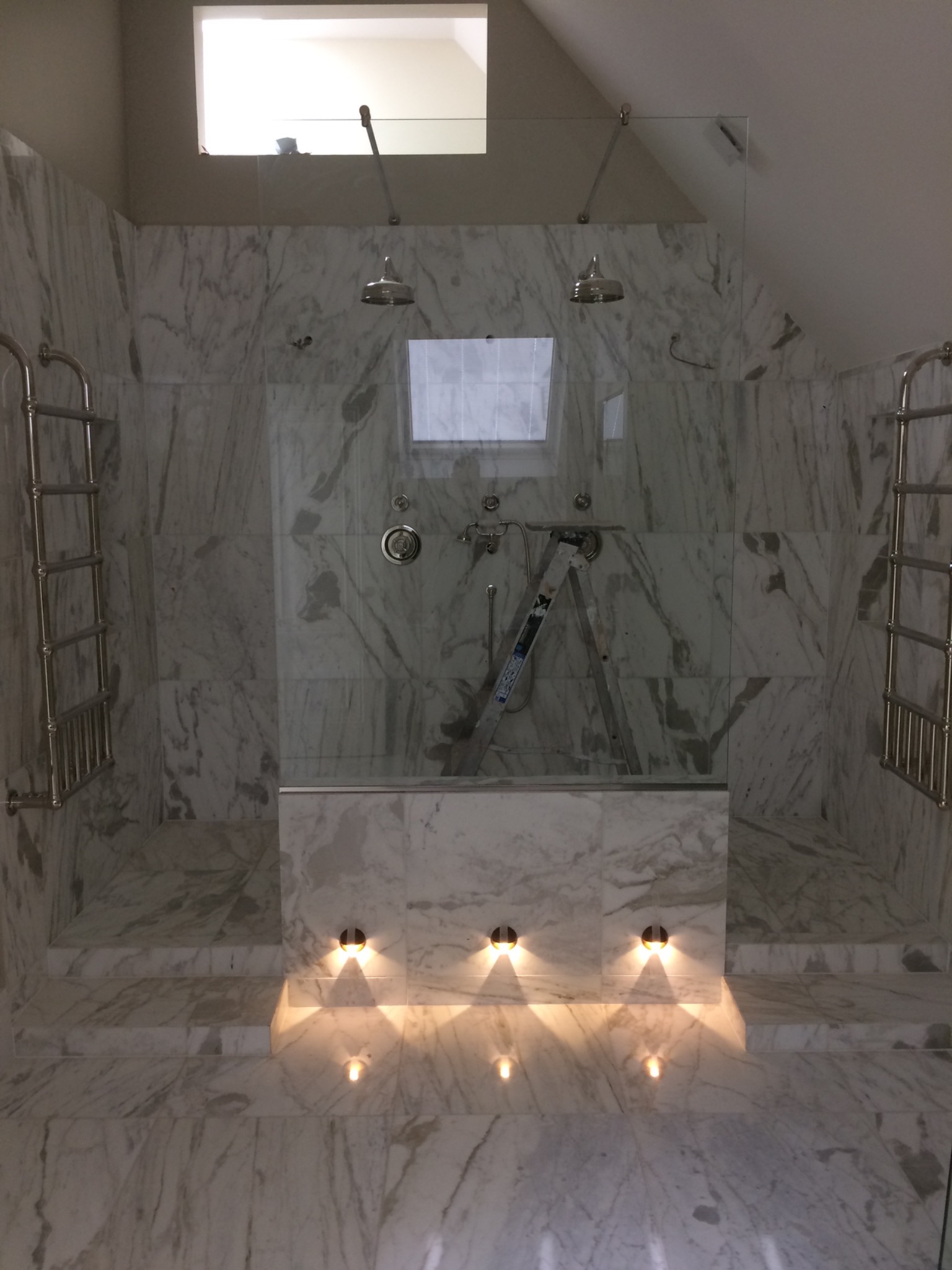 Łazienka w trakcie montażu kabiny prysznicowej z marmurowymi ścianami, widoczna drabina monterska i punktowe oświetlenie podłogowe.