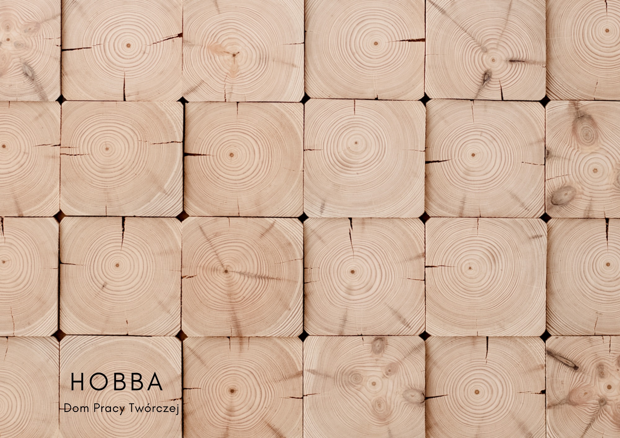 Drewniana ściana z kwadratowych bali z widocznymi słojami, logo 'HOBBA Dom Pracy Twórczej' w lewym dolnym rogu.