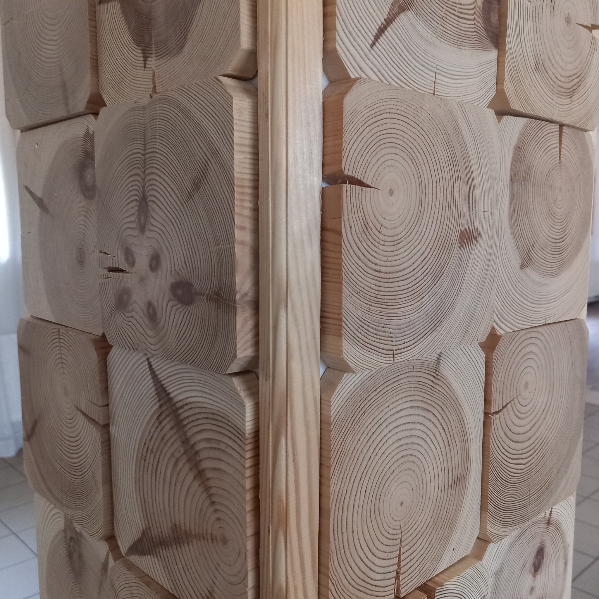 Ściana z drewnianych, kwadratowych bali z widocznymi słojami, połączonych drewnianą listwą.