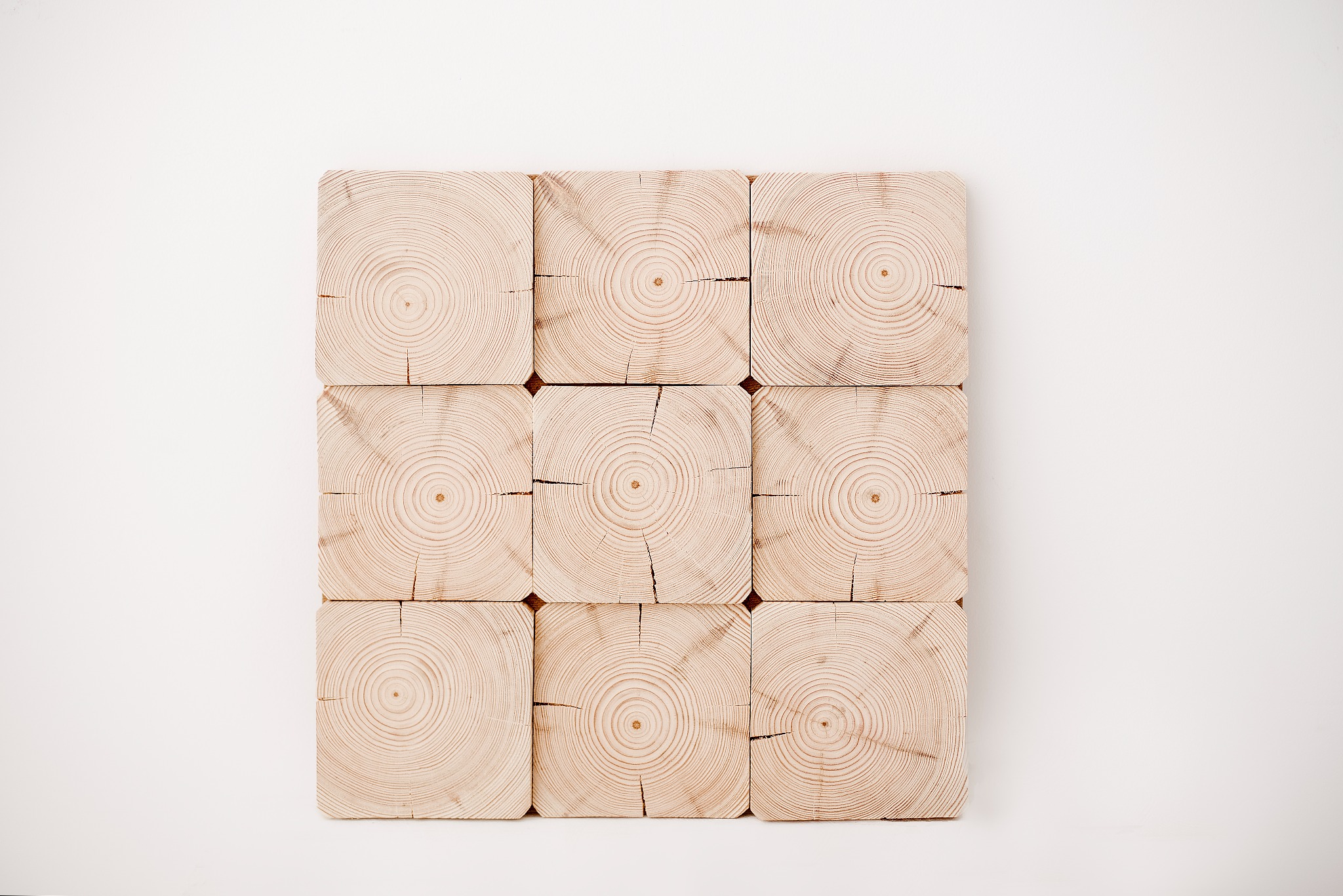 Dekoracyjna ściana z dziewięciu kwadratowych bloków drewna z widocznymi słojami, ułożonych w regularną siatkę na białym tle.