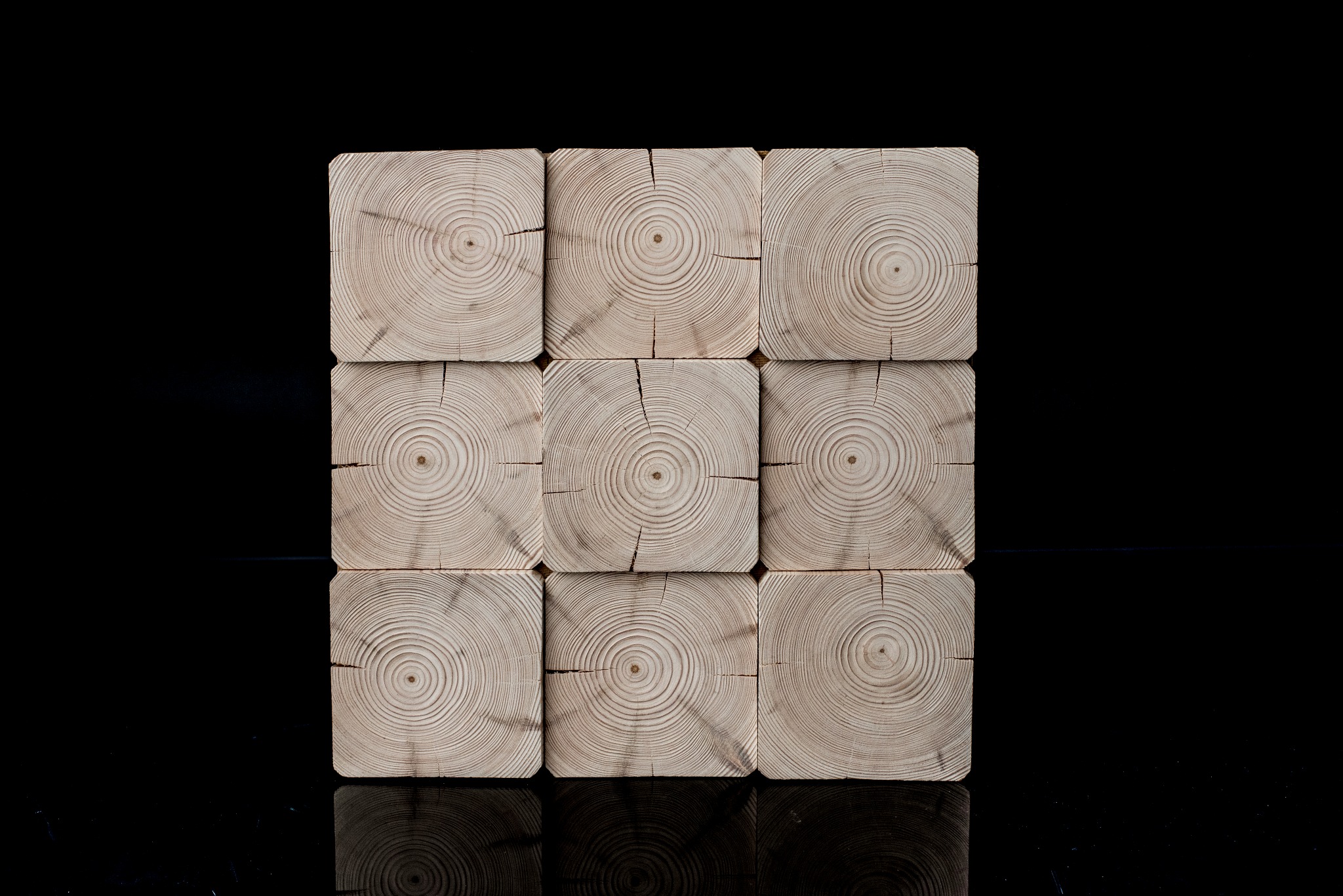 Precyzyjnie ułożone, surowe, kwadratowe bale drewniane z widocznymi słojami, tworzące regularną strukturę na błyszczącym czarnym tle.