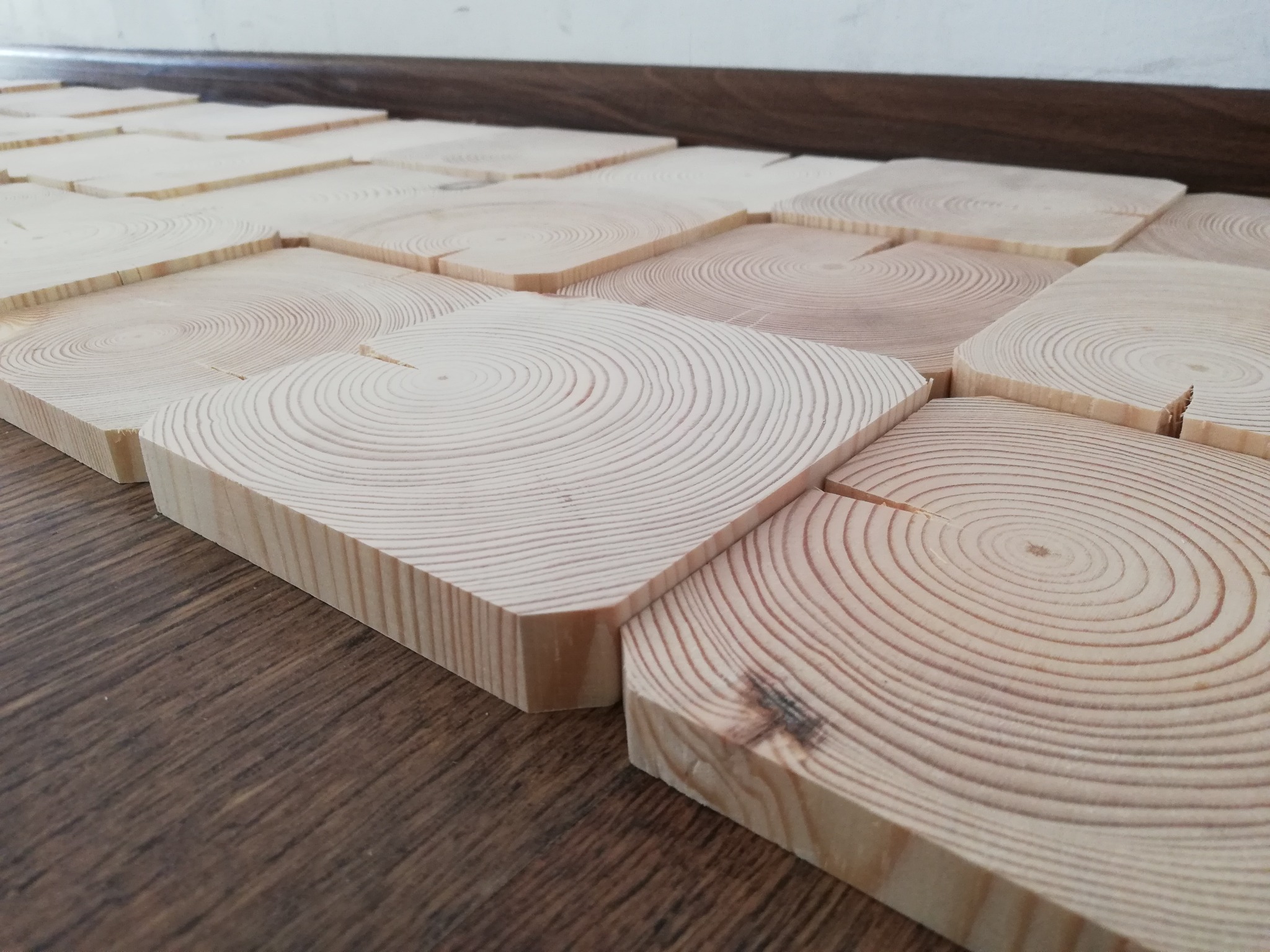 Ułożone kwadratowe płytki podłogowe z jasnego drewna z widocznymi słojami, na ciemnobrązowej podłodze laminowanej, z bliska.