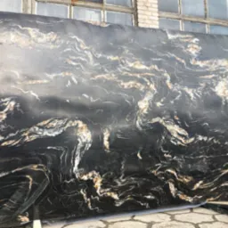 Duża płyta czarnego kamienia z wyraźnymi, falistymi żyłami w kolorach bieli i złota, oparta o ceglany budynek z oknami.