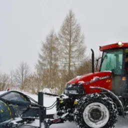 Czerwony traktor Case IH 95 z pługiem STARK odśnieża teren w zimowy dzień, widoczne opady śniegu i drzewa w tle.