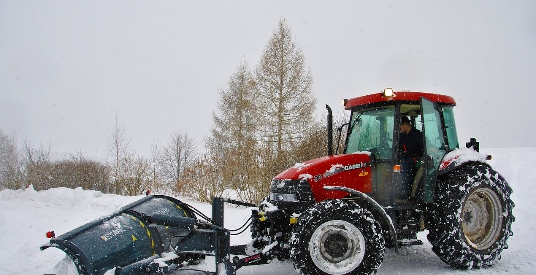 Czerwony traktor Case IH 95 z pługiem STARK odśnieża teren w zimowy dzień, widoczne opady śniegu i drzewa w tle.
