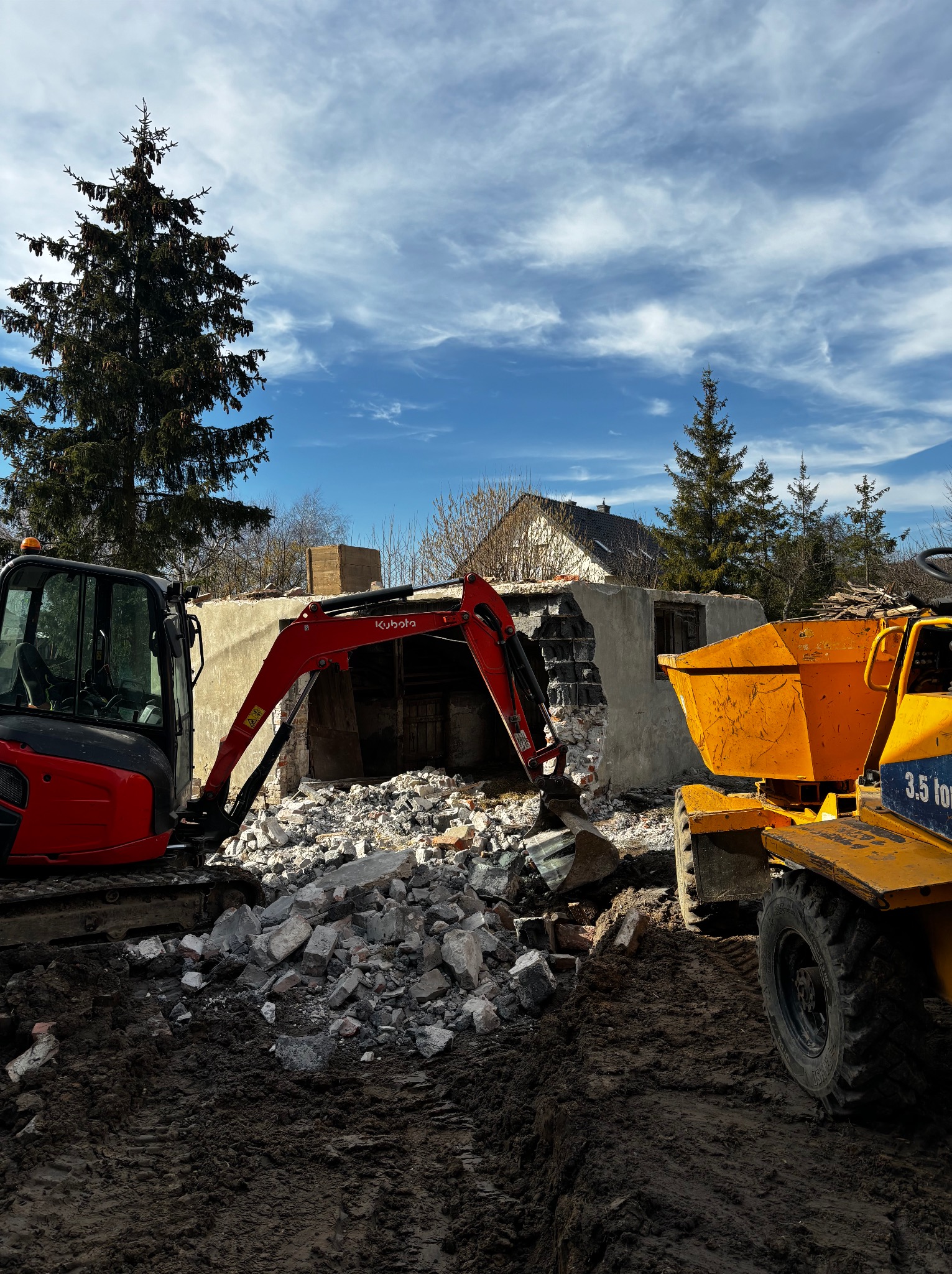 Czerwona mini koparka Kubota i wywrotka 3.5 tony podczas rozbiórki budynku w Krzeszowicach. Gruz na ziemi, błękitne niebo w tle.