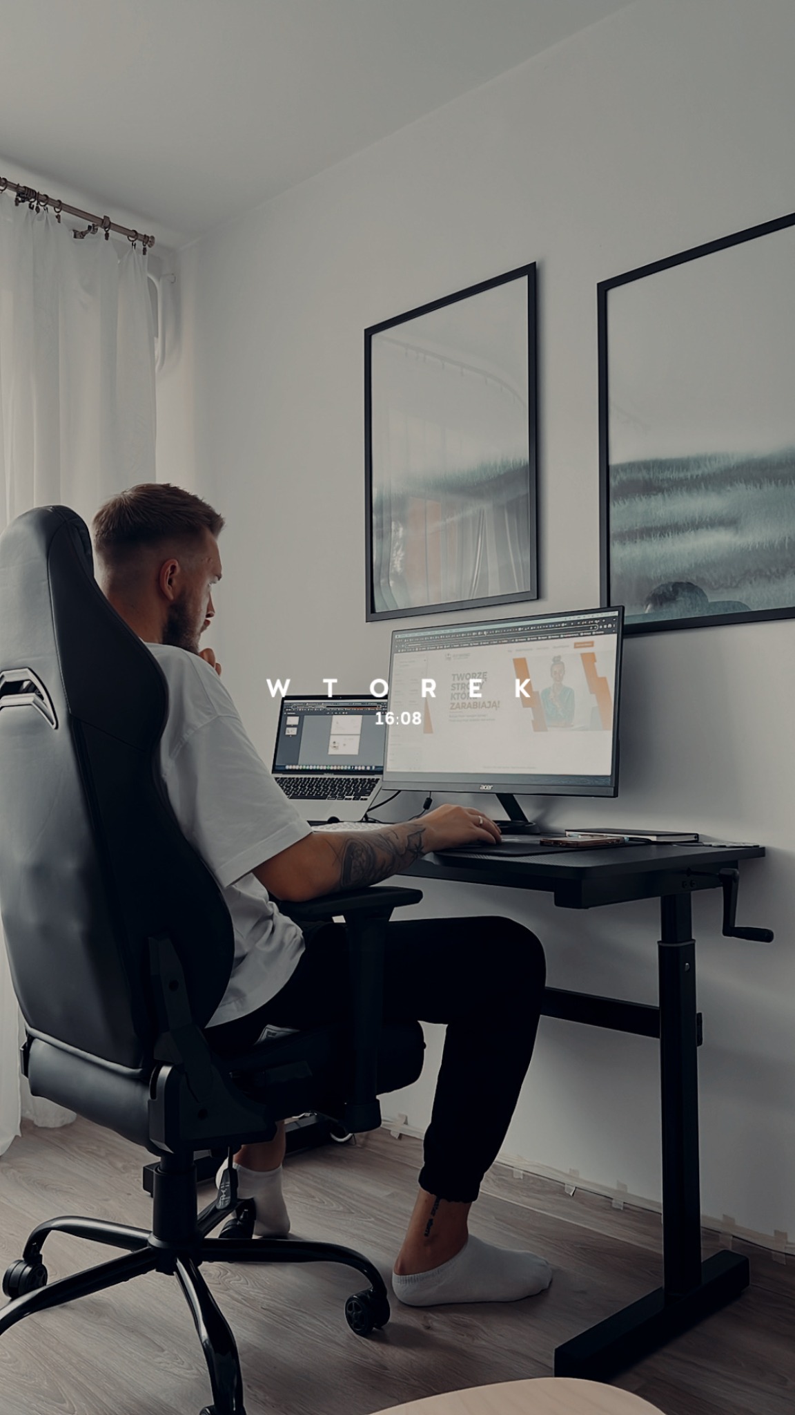 Mężczyzna z tatuażem na ramieniu siedzi na krześle biurowym przed biurkiem z dwoma monitorami, na jednym z nich widoczna strona internetowa z hasłem 'Tworzę strony, które zarabiają'.