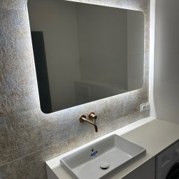 REMOSFERA MYKHAILO HRYN - Nowoczesna łazienka we Wrocławiu: umywalka Roca, bateria w kolorze miedzi i podświetlane lustro na tle płytek imitujących kamień.