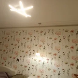 Kwiatowa tapeta w pokoju we Wrocławiu z nowoczesnym oświetleniem sufitowym w kształcie gwiazdy i wiszącą lampą.