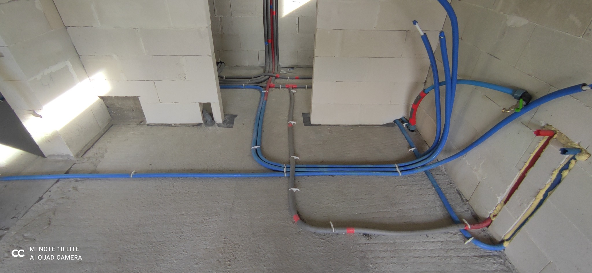 Surowe wnętrze z widocznymi rurami instalacji wodnej i grzewczej, częściowo ukrytymi w ścianach z betonu komórkowego, zabezpieczonymi pianką montażową i spiętymi plastikowymi opaskami.