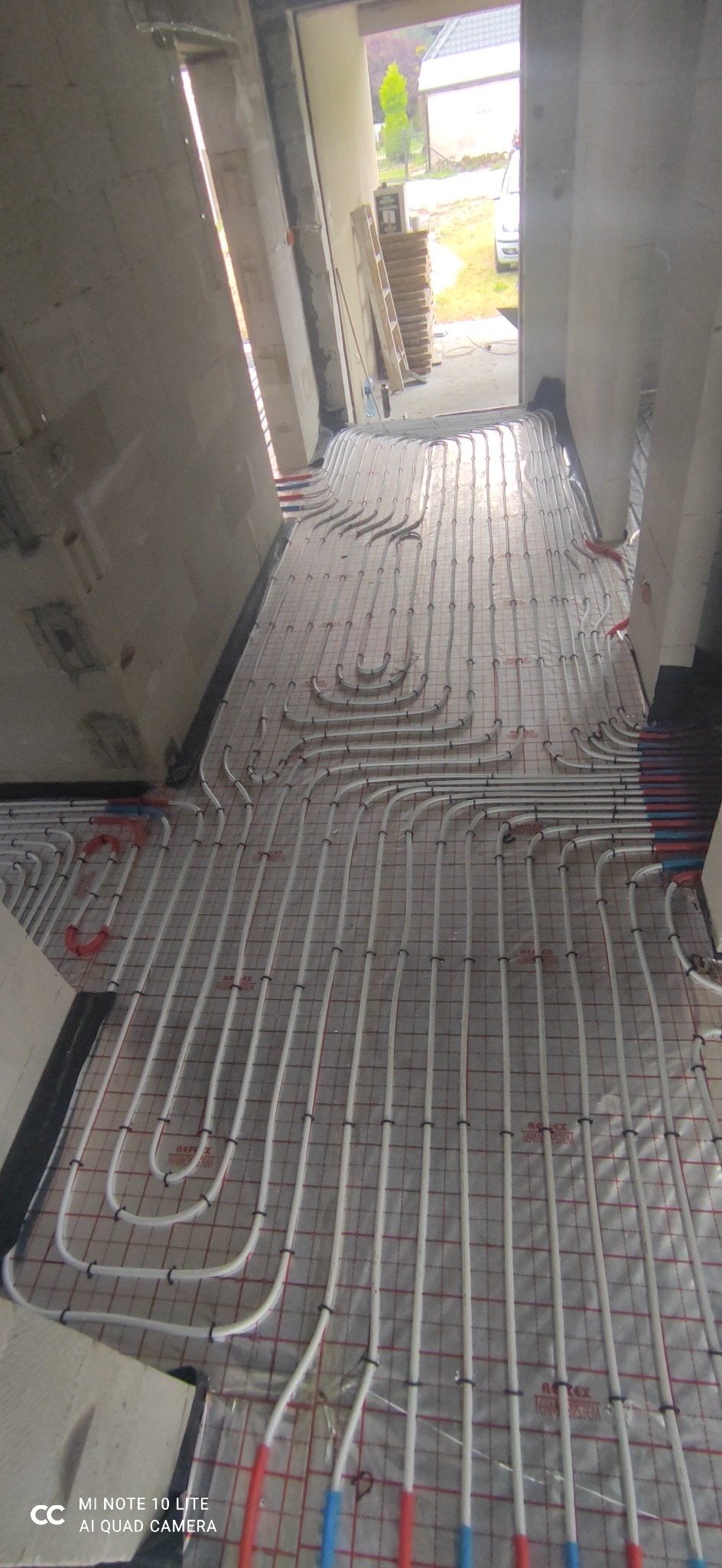 Rozłożone rury ogrzewania podłogowego na folii z siatką w surowym wnętrzu budynku w trakcie budowy, widok z góry.