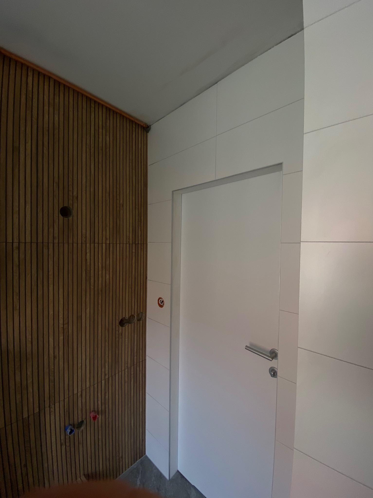 Nowoczesna łazienka w trakcie wykańczania: drewniana boazeria, białe płytki i drzwi. Widoczne przyłącza wodne.