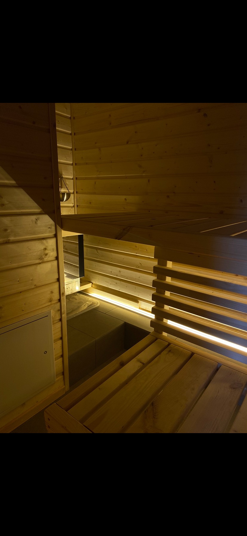 Drewniana sauna z podświetlanymi ławkami i metalowym czerpakiem. Widoczne deski boazeryjne i konstrukcja sauny w ciepłym oświetleniu.