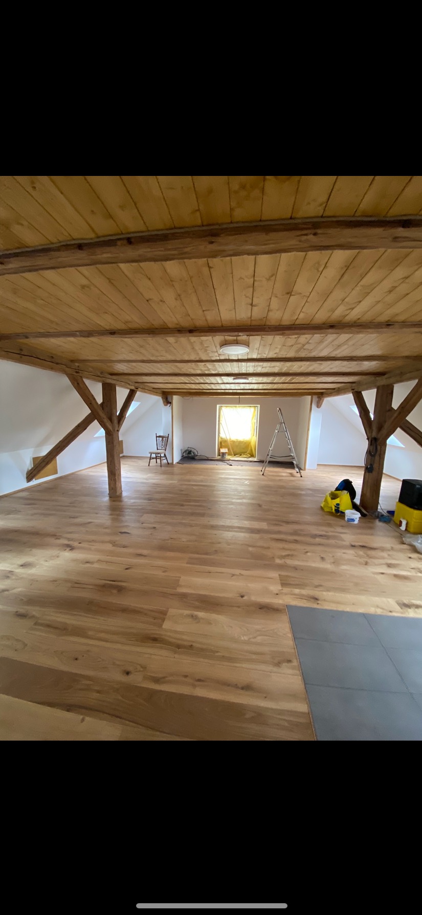 Jasne panele podłogowe w przestronnym, drewnianym poddaszu z widocznymi belkami stropowymi i elementami wyposażenia, takimi jak drabina i krzesło.