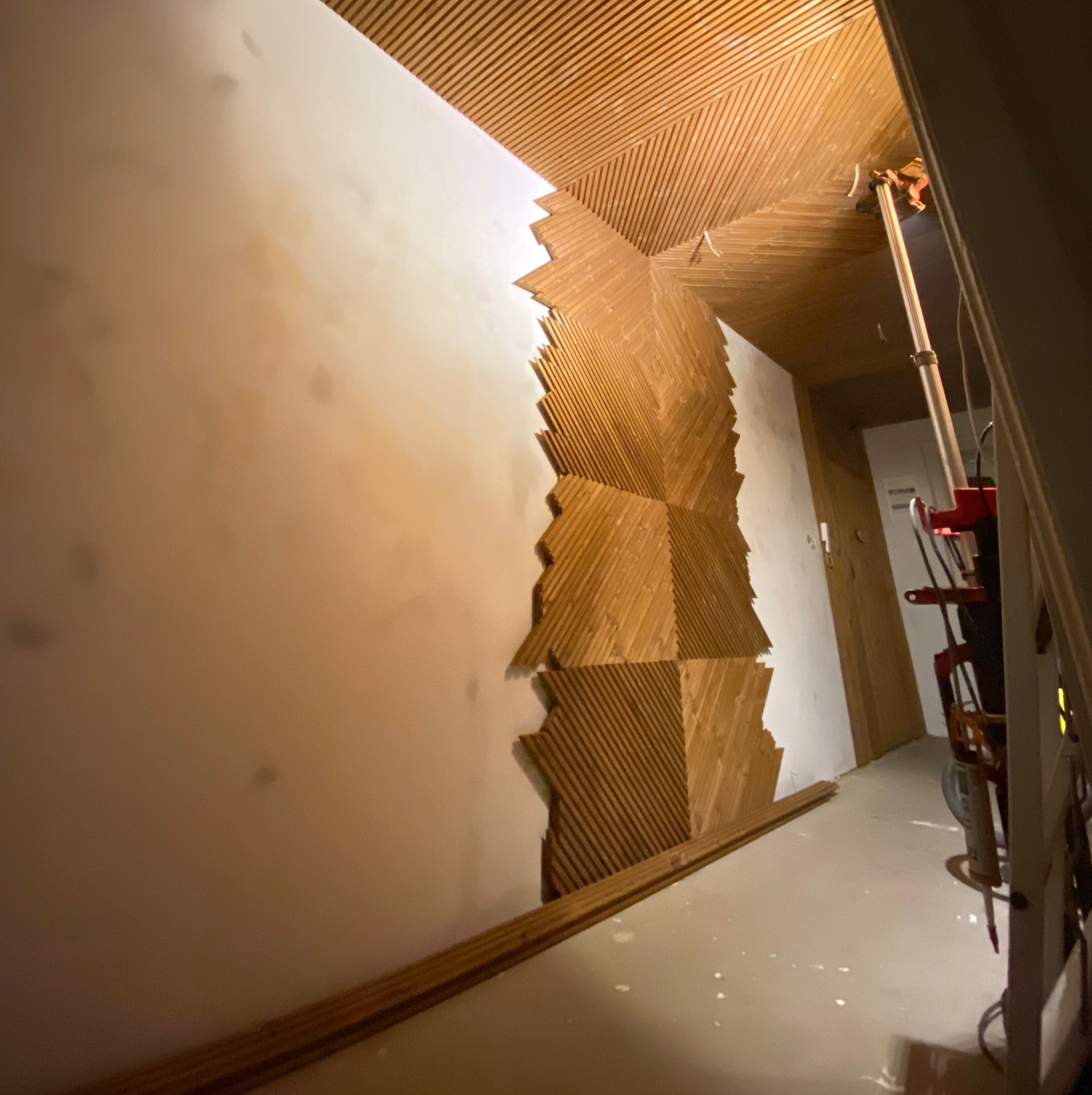 Montaż dekoracyjnej, drewnianej boazerii na ścianie, widok na fragment sufitu z drewnianymi listwami. W tle widoczny sprzęt budowlany.