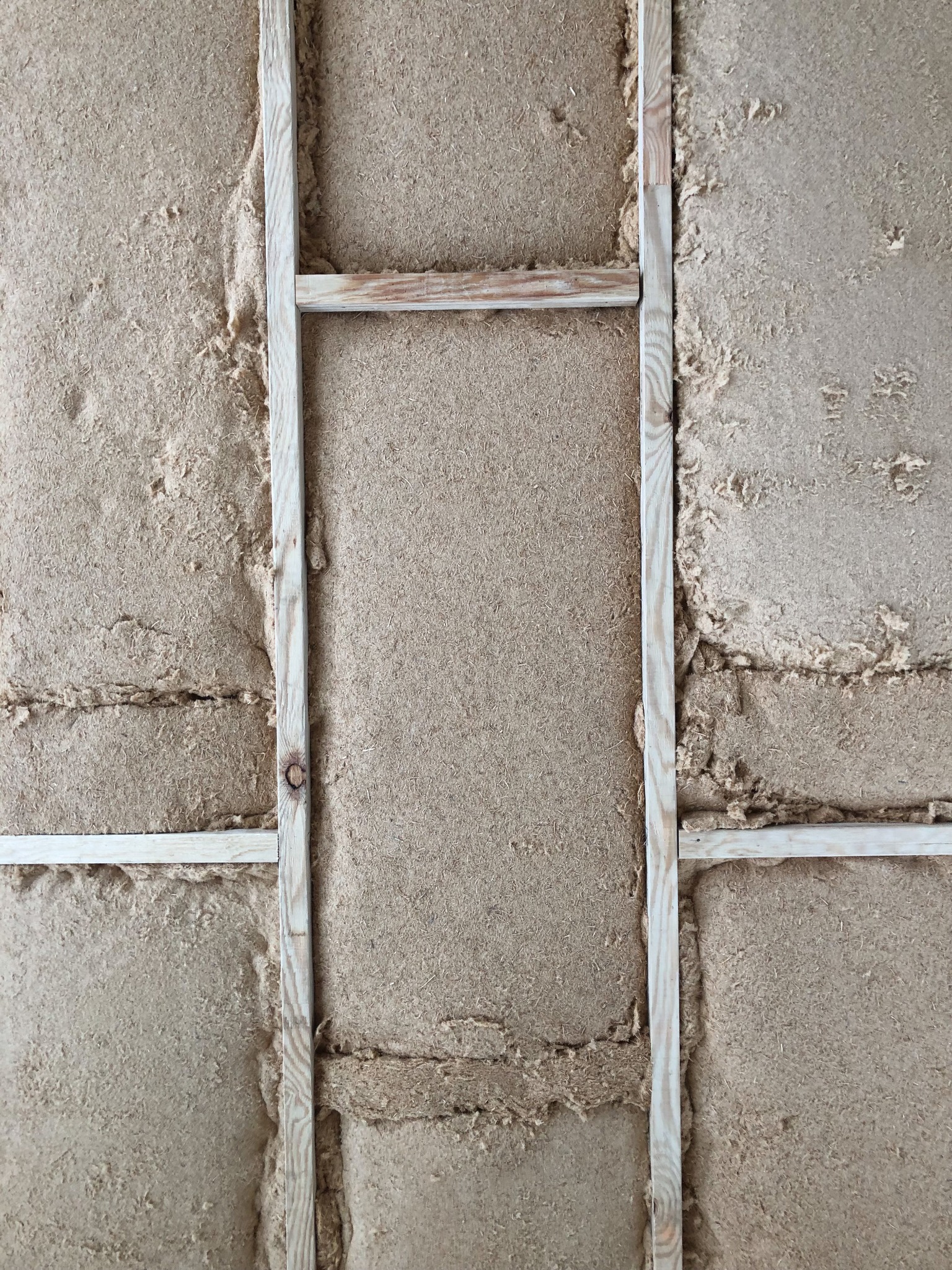 Fragment ściany z izolacją z włókien naturalnych, widoczne drewniane elementy konstrukcyjne w trakcie montażu.