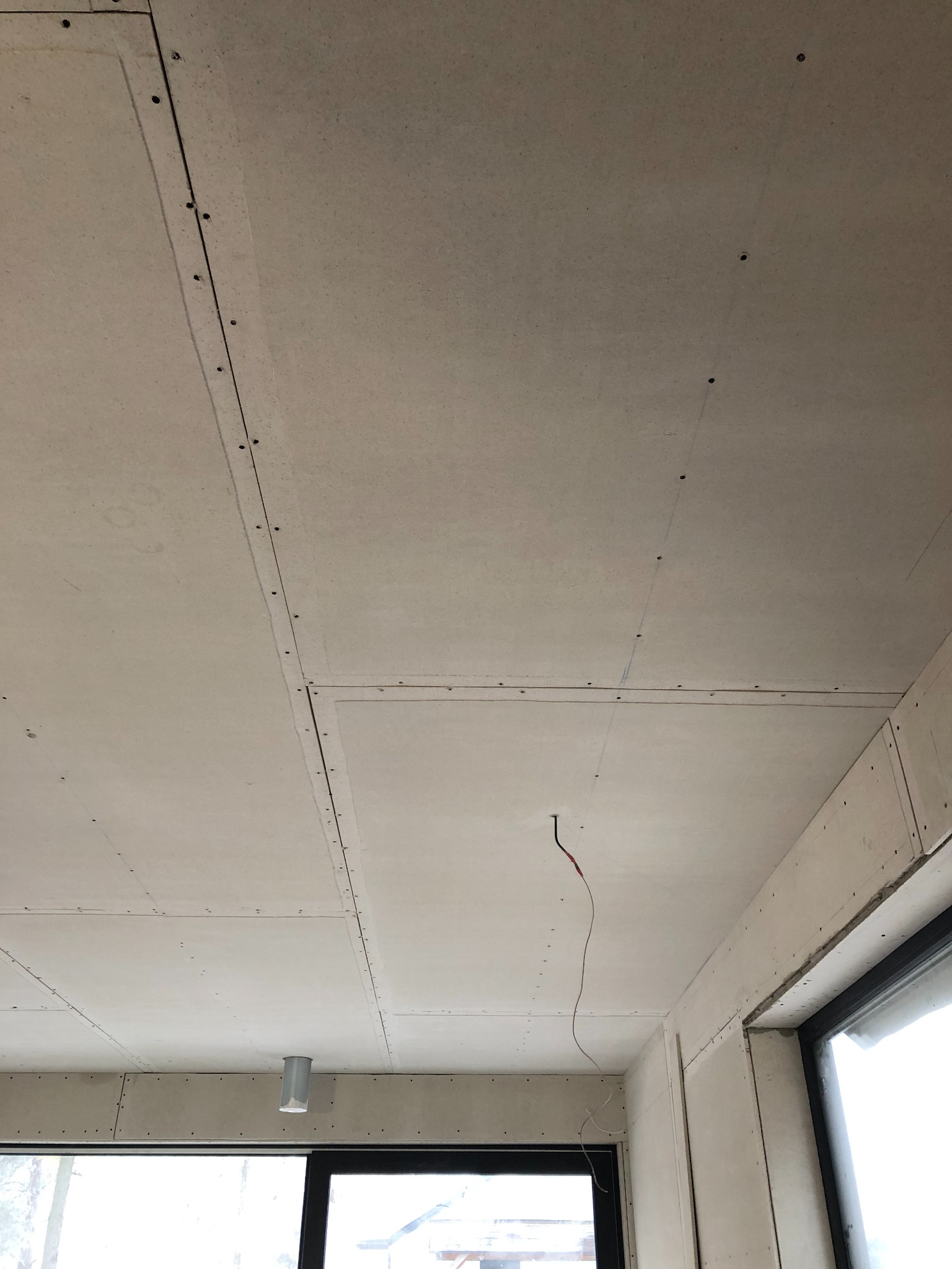 Montaż płyt gipsowo-kartonowych na suficie, widoczne łączenia płyt i wystający kabel elektryczny, okno w tle.