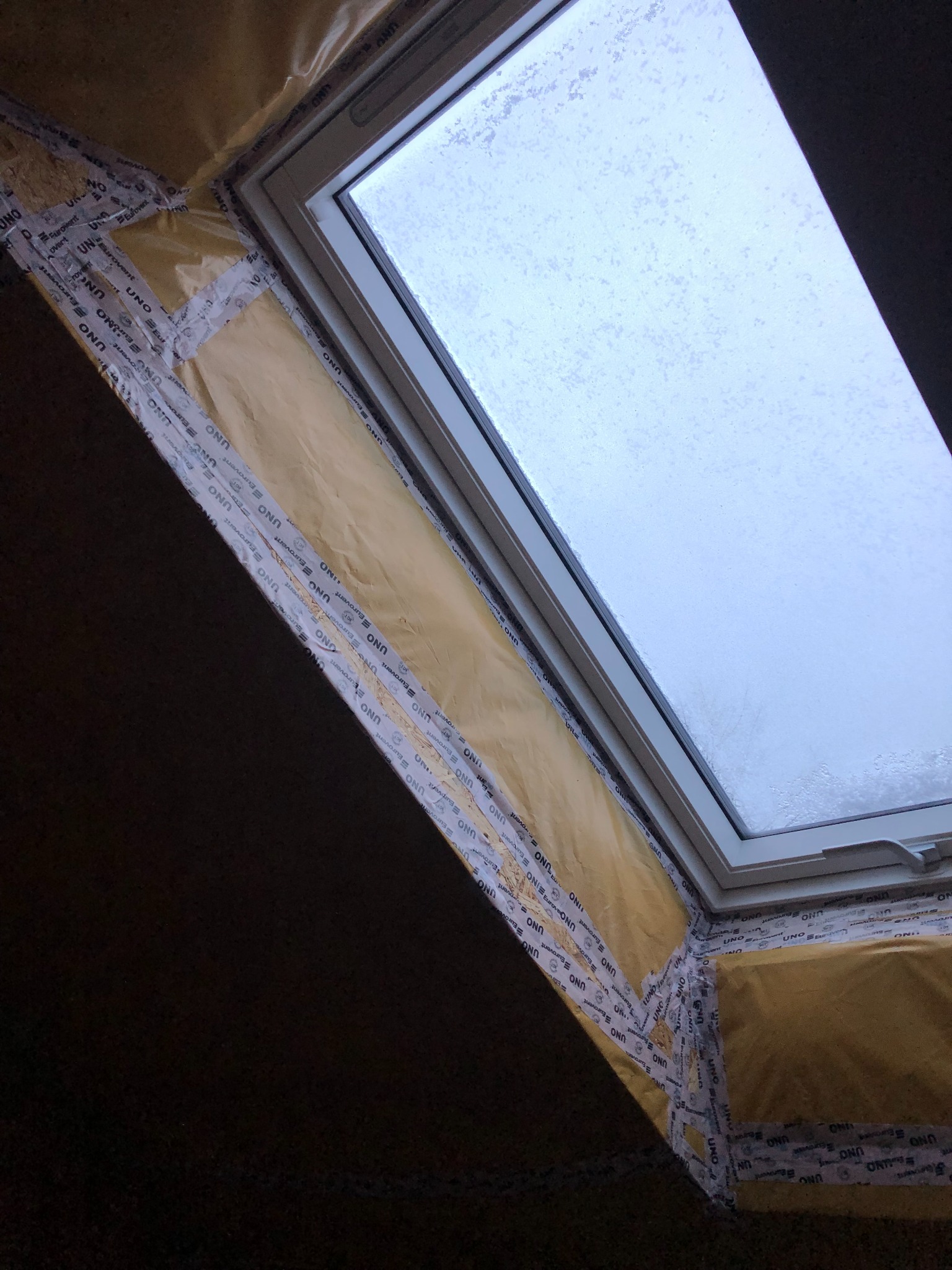 Izolacja poddasza z oknem dachowym w trakcie montażu, widoczne folia paroizolacyjna i taśma uszczelniająca na łączeniach.