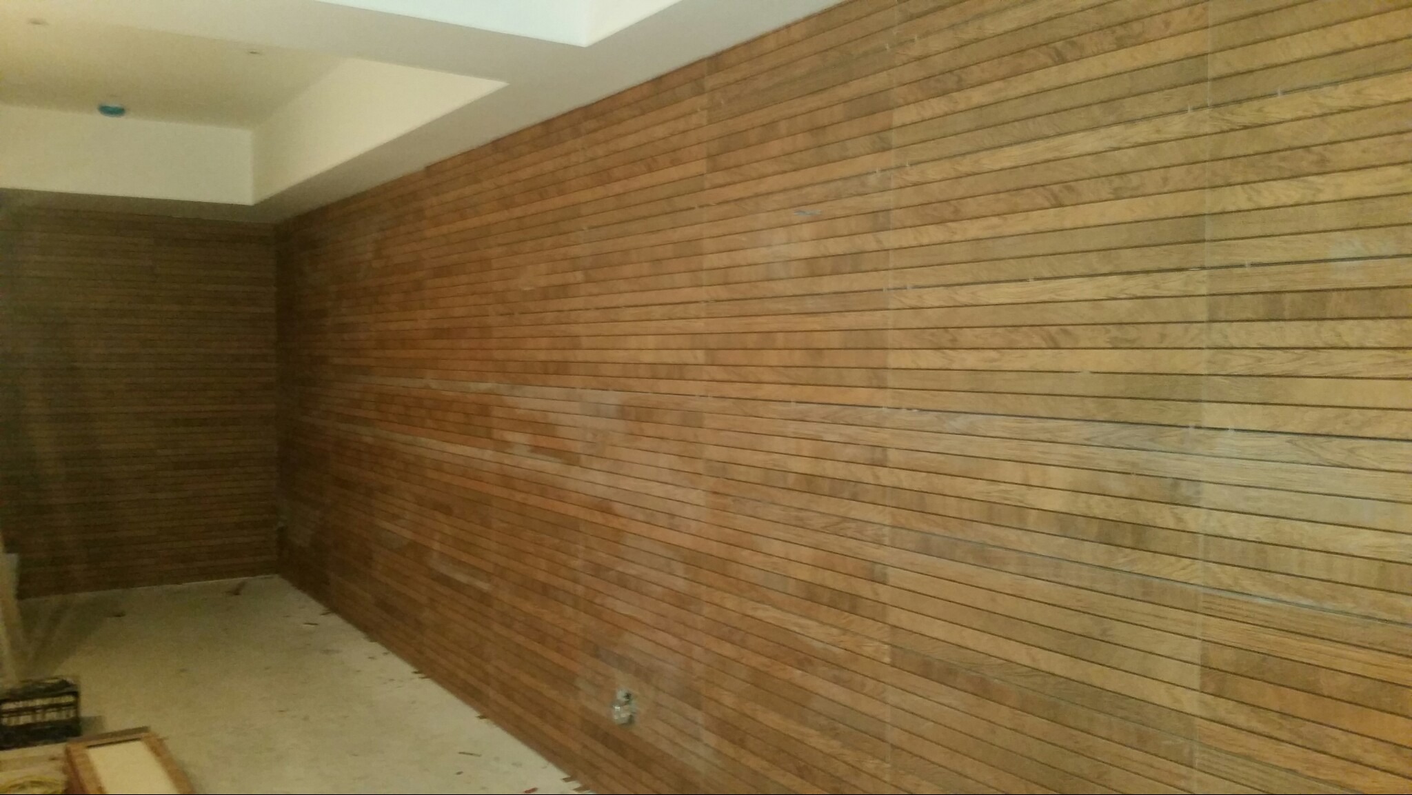 Ściana wykończona panelami drewnopodobnymi w Trzciance, z widocznymi drobnymi niedoskonałościami na łączeniach, surowy stan wykończenia wnętrza.