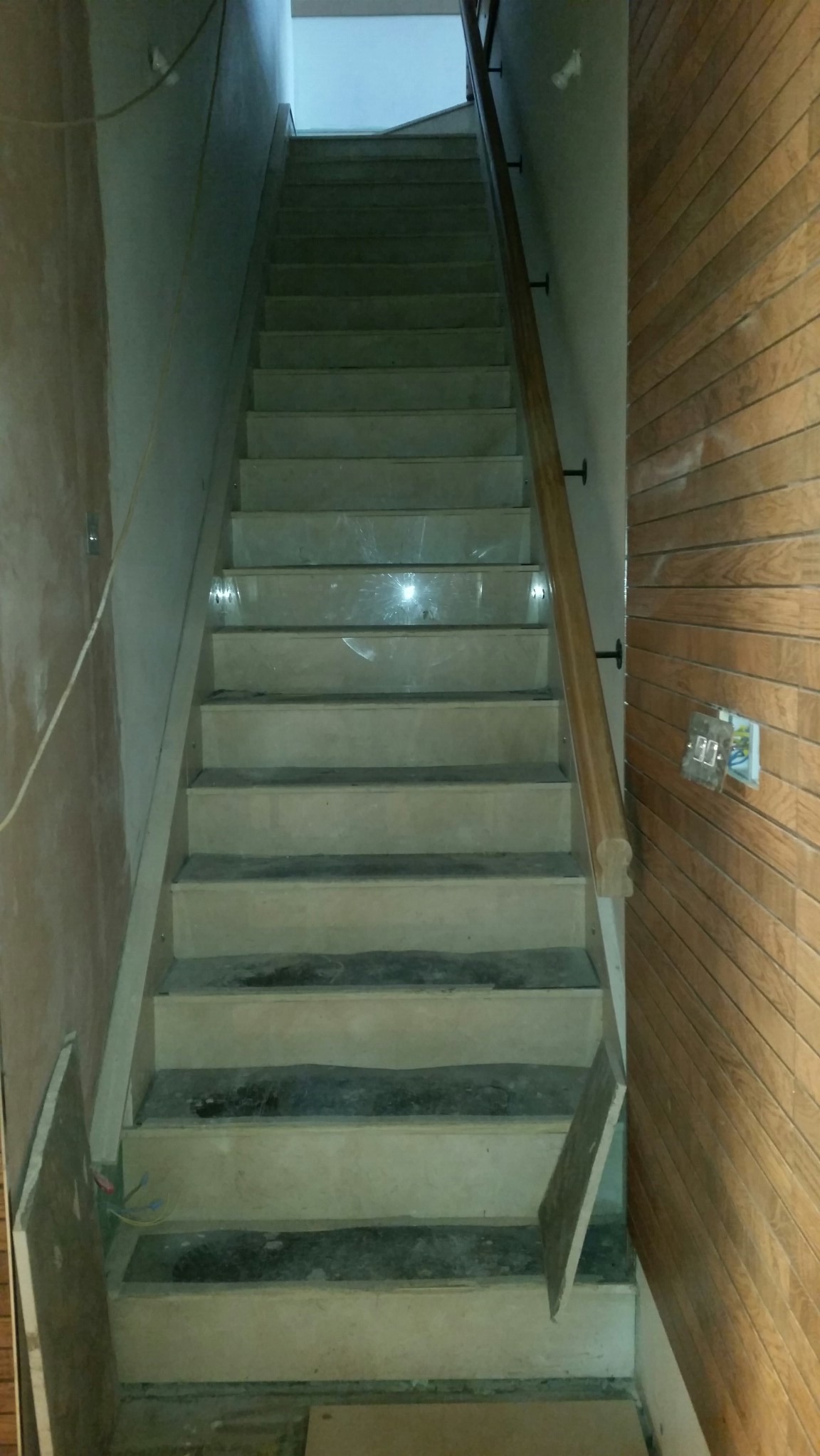 Schody wewnętrzne w trakcie remontu, widoczne surowe ściany, drewniana balustrada i zabezpieczone folią schody.