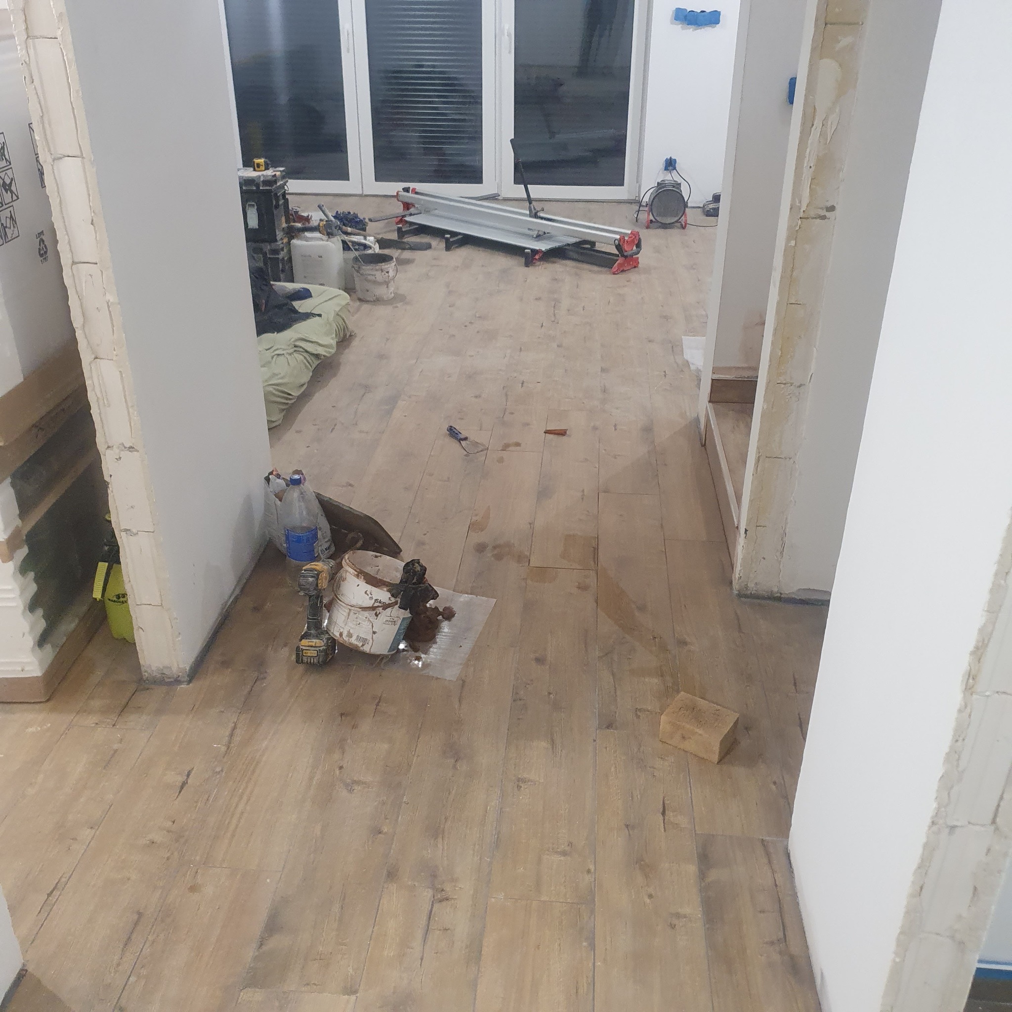 Rozłożone panele podłogowe z widocznymi narzędziami i akcesoriami do montażu, w tle okno balkonowe i przygotowane ściany do dalszych prac wykończeniowych.