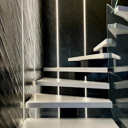 MSN Dawid Lorenc - Nowoczesne schody z drewnianymi stopniami, szklaną balustradą i oświetleniem LED na ścianie o teksturze kamienia.