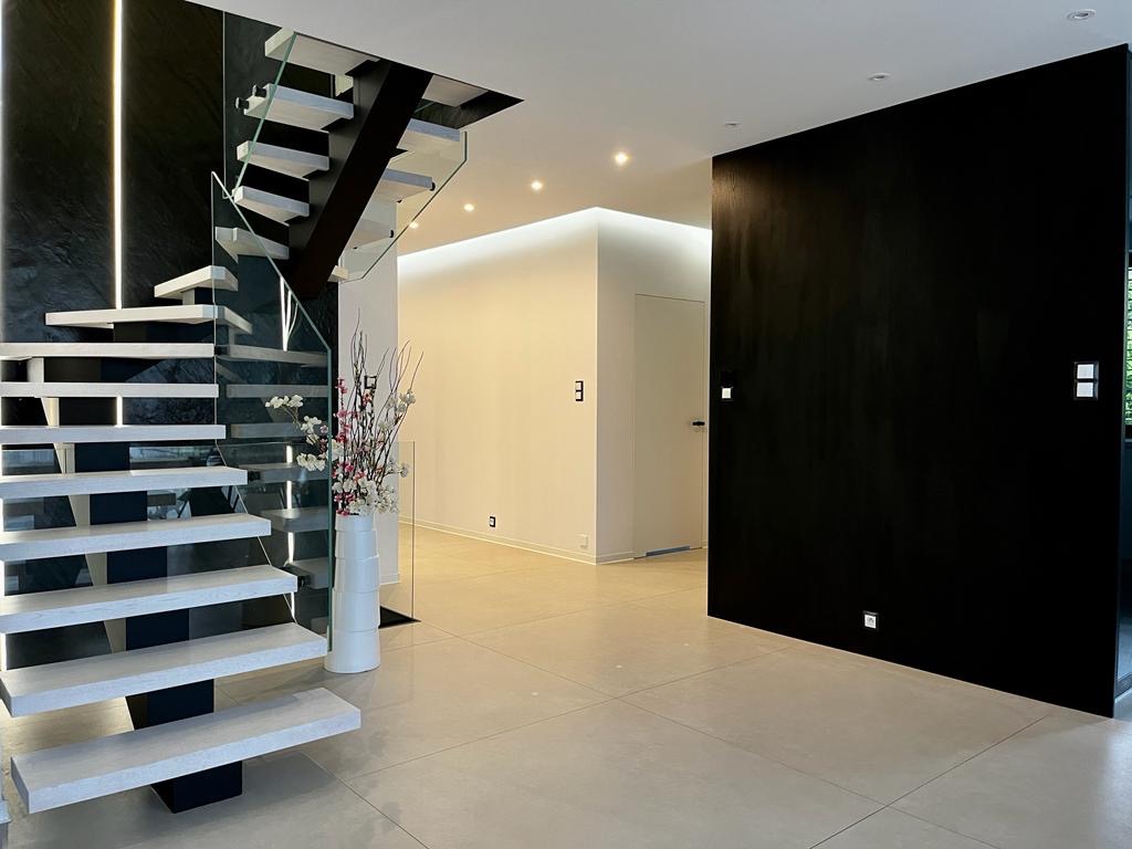 Nowoczesne schody wspornikowe z białymi stopniami i szklaną balustradą, czarny marmur na ścianie, minimalistyczny wystrój wnętrza z białymi i czarnymi elementami.