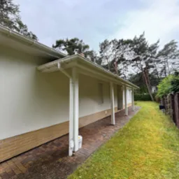 Jasny dom jednorodzinny z białymi kolumnami werandy i elewacją w odcieniach beżu, widok z boku na tle zielonego trawnika i drzew