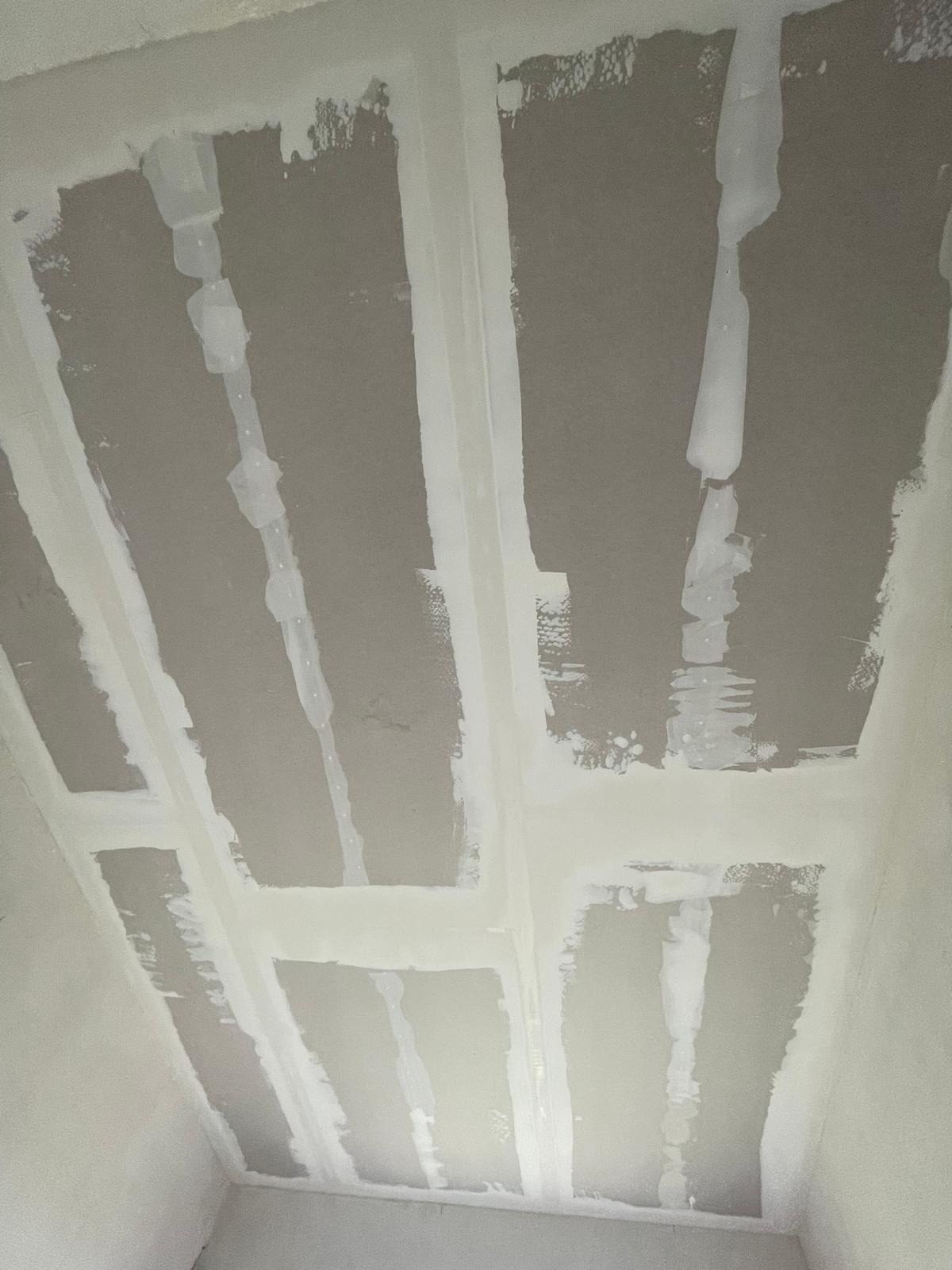 Sufit z płyt kartonowo-gipsowych, na którym widoczne są świeżo nałożone spoiny i taśmy wzmacniające, przygotowane do dalszego szpachlowania.