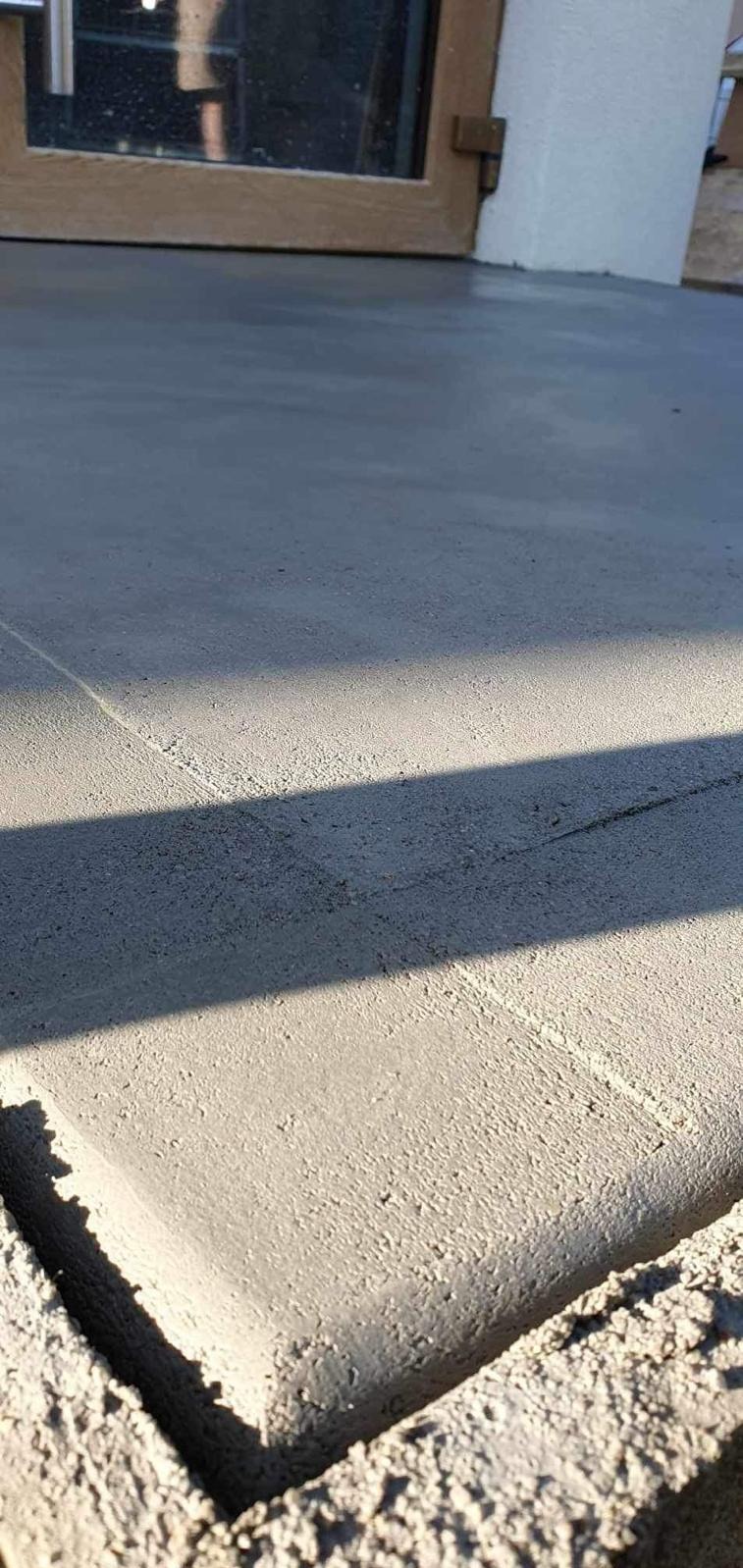 Świeżo wylana, gładka, szara wylewka betonowa pod progiem okiennym, z widocznym cieniem rzucanym przez element konstrukcyjny.