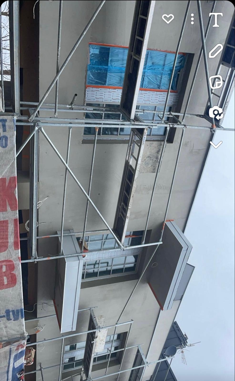 Elewacja budynku w trakcie prac, widoczne rusztowania, okna zabezpieczone folią, ściana po tynkowaniu, przygotowana do dalszych prac wykończeniowych.