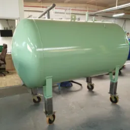 Jasnozielony, poziomy zbiornik ciśnieniowy na kółkach w hali produkcyjnej w Kaliszu, widoczne inne zbiorniki i stanowisko komputerowe w tle.