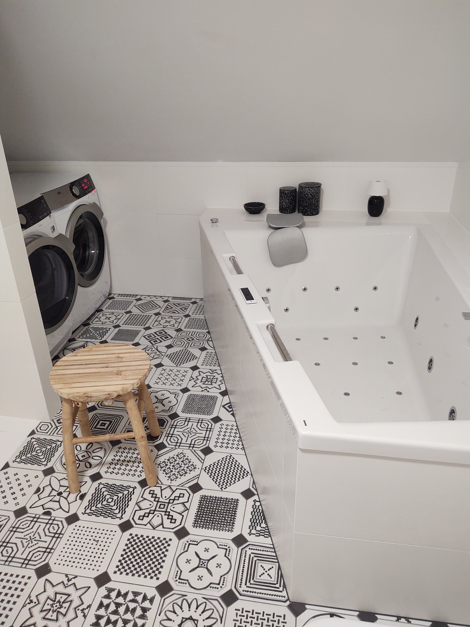 Wykończona łazienka w Stargardzie z wanną z hydromasażem, wzorzystą podłogą i pralką w rogu, podkreślona drewnianym stołkiem.