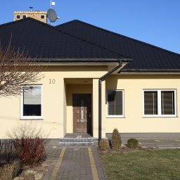 Bogusława Trela Fotografia - Elewacja domu jednorodzinnego z czarnym dachem i numerem 10 nad wejściem, widziana z poziomu chodnika.